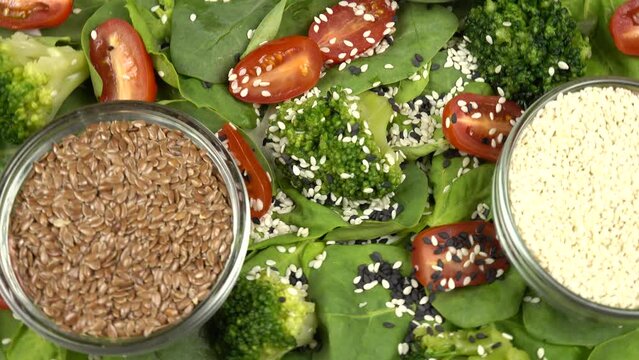 Nutrient seeds.  Flax seeds, black and white sesame seeds in glass bowls and a vegetable salad of spinach leaves, broccoli and cherry tomatoes