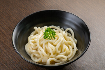 A bowl of udon noodles on a wooden table.
