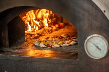 A pizzaiolo is making pizza in a wood fired oven