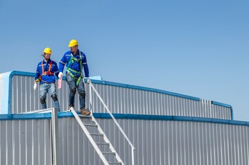 Two construction workers wearing safety gear are working on the roof of a building.