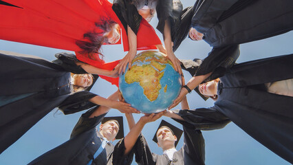 College graduates stand in a circle and hold a geographical globe of the world.