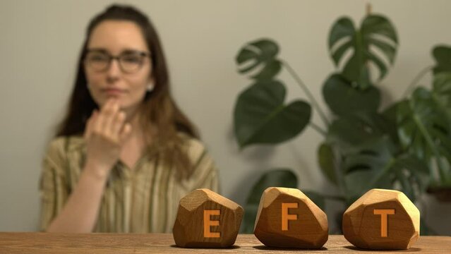 Letters EFT writen on irregular wooden blocks. Female tapping chin (CH) meridian point in blurred background. Emotion-focused therapy treatment concept.