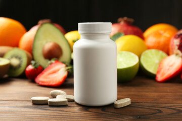 Vitamin pills, bottle and fresh fruits on wooden table