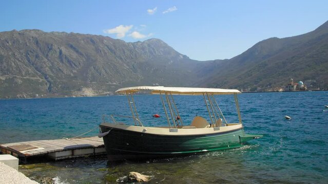 A boat standing at a wooden pier rocking on the waves. The Adriatic sea. Perast. Montenegro. The bay of Kotor.