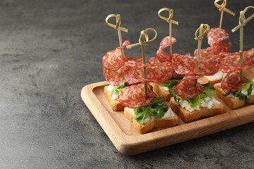 Tasty canapes with salami, greens and cream cheese on grey table. Space for text