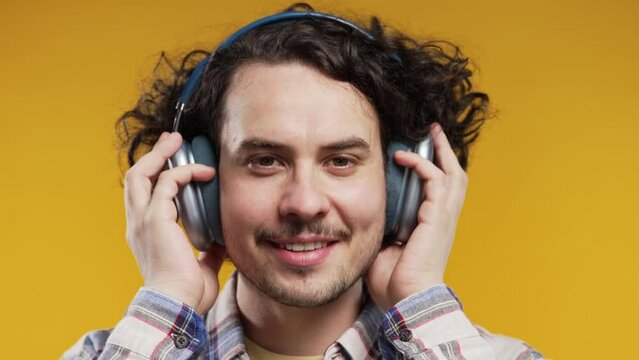 Positive curly haired man listening music, enjoying dance with modern headphones