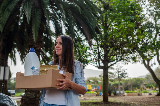 A woman is holding a cardboard box and a bottle of water. She is smiling and she is happy