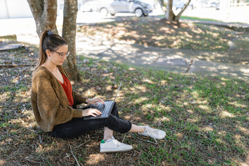 Confident lady wearing sneakers using laptop to work remotely in park