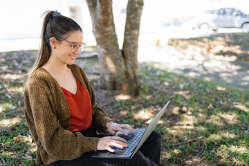 Cheerful lady in glasses sitting on ground and working with laptop