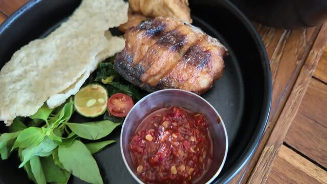 Traditional Indonesian dish grilled mackerel fish with white rice, vegetables and sambal on black plate. Concept for restaurant and eatery.