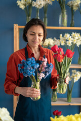 female florist in her flower shop holding two vases with flowers, tulips and hyacinths. Spring