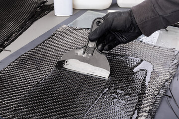 hand working epoxy resin into woven carbon fiber reinforcement cloth. Production manufacturing of ...
