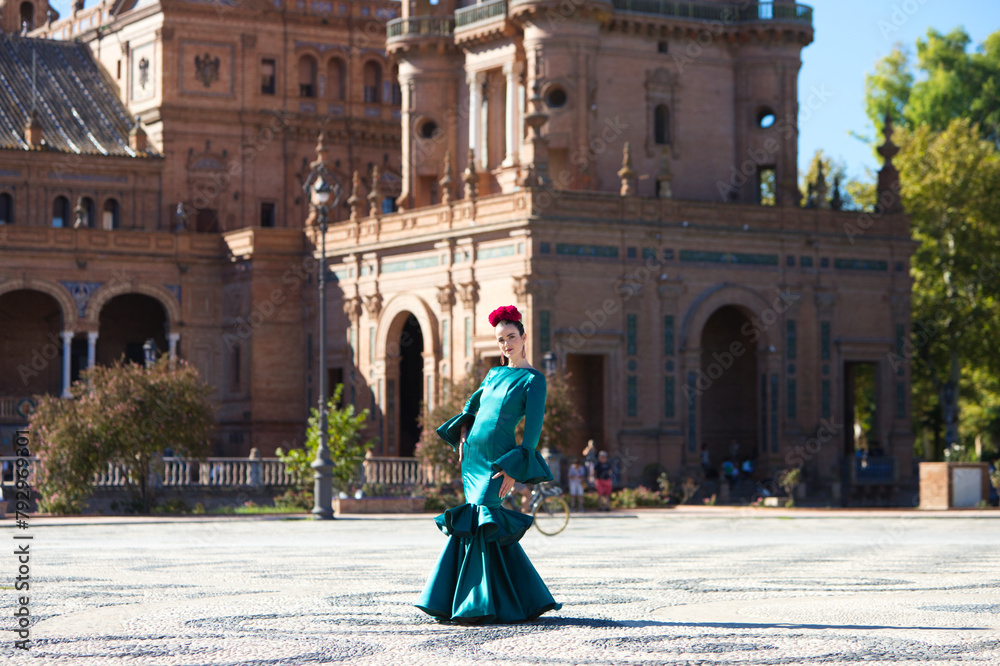 Wall mural young and beautiful woman with typical green dress with ruffles and dancing flamenco in plaza de esp