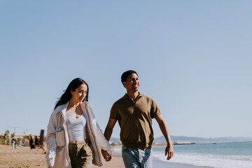 Joyful couple running hand in hand along a sunlit beach in Barcelona, Spain