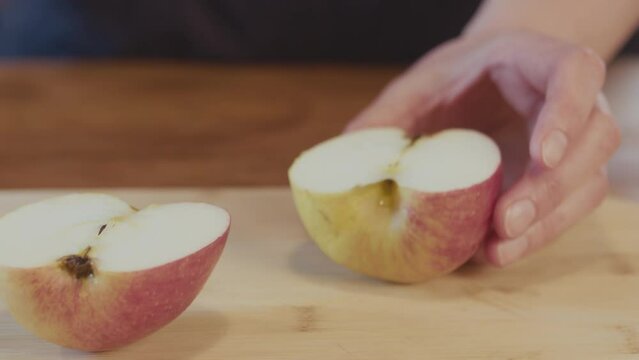 Woman placing an apple on a wooden board and cutting it in half,. Handheld studio shot. Studio lighting. Interior. Kitchen. Close up. High quality 4k footage