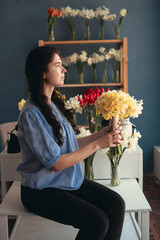 Florist holding a bouquet of daffodils sitting in a flower shop looking out the window enjoying the moment