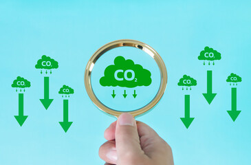 Hand holding a magnifying glass with symbol reducing carbon dioxide emissions to limit global warming and sustainable development and green business concept.