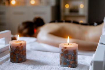 Burning candles in the foreground. Woman enjoying hot stone massage at spa salon. Professional masseur making stone therapy. Relaxing and ease tense muscles and damaged soft tissues throughout body. - obrazy, fototapety, plakaty