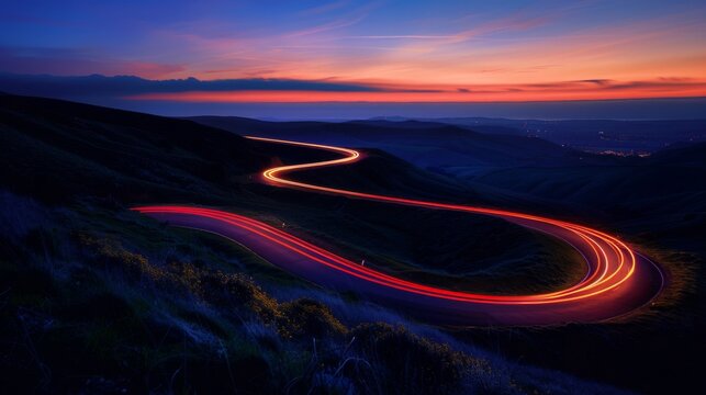 A winding road illuminated by car headlights against the backdrop of a twilight sky