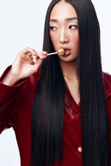 Fototapeta premium Attractive woman with long black hair and red jacket playfully holding a spoon in her mouth
