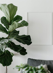 Close-up of a large house plant with large leaves next to a blank vertical poster in a white frame on a white wall hanging above a chair with a gray upholstered cushion.