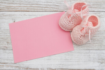 Pink baby booties with pink greeting card on weathered wood