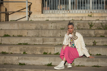 Young, pretty, blonde woman, with blue eyes, white fringed jacket and pink skirt, with her hand on...