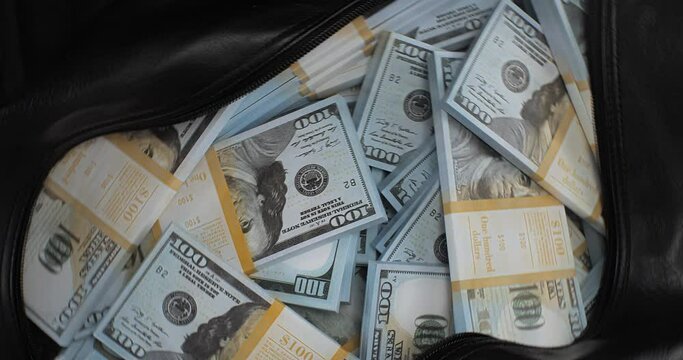 Close-up of a rotating bag with a lot of dollars money. A large amount of money in a travel bag on a black background. Money in a bag of a stack of hundred dollar bills.