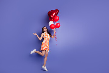 Full size photo of pretty young woman overjoyed jump hold balloons empty space wear dress isolated on violet color background