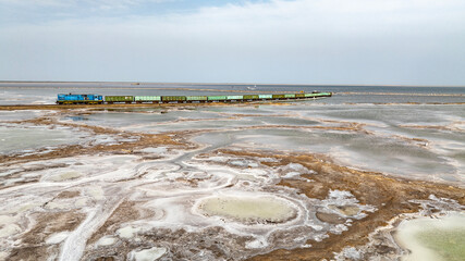 a train travels across a salt lake to transport salt in the area of Lake Baskunchak on a spring day