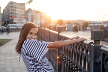 A  beautiful teenage girl walks around the city against the background of sunlight, the model...