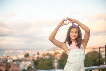 Portrait of a beautiful girl against the background of the roofs of the city. The model makes heart