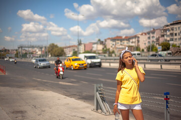 A girl in a yellow t-shirt calls taxy, standing on the road  against the cars