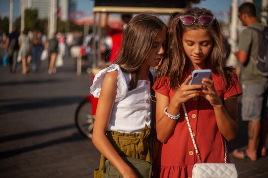 Two cute gitls are looking to the phone on a busy street in the city