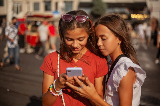 Two cute gitls are looking to the phone on a busy street in the city