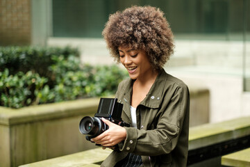 Happy female photographer taking a picture with an analog camera outside.