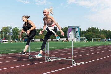 Two athlete woman runnner running hurdles at the stadium outdoors