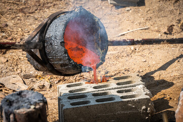 Blacksmith holding a hot crucible by the iron pliers from furnace and pouring the melting gold into the statue block.