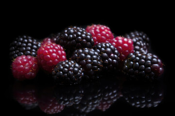 Some red and black fresh blackberries on black background with reflection. Organic farm food, natural forest berries, fresh market, healthy products.