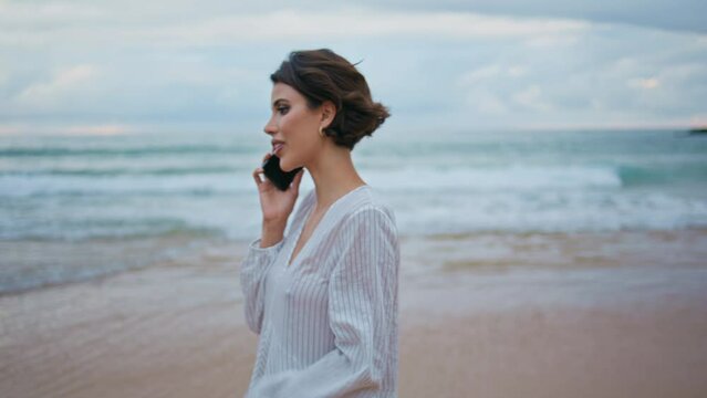 Friendly girl talking cellphone at beautiful ocean waves. Calm model going shore