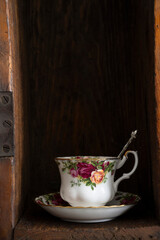Teacup and saucer decorated with flowers and silver teaspoon in wooden box