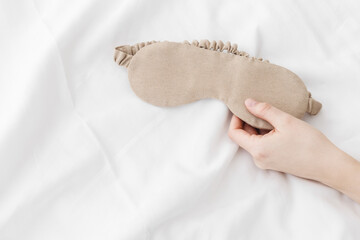 Beige eye mask for sleep on bed background, minimal lifestyle aesthetic, copy space. Top view woman...
