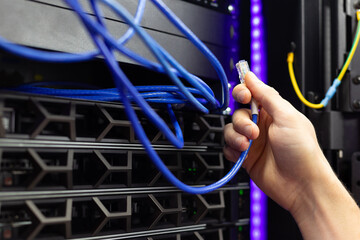An engineer in a server room connects a cable to the data center. IT technology