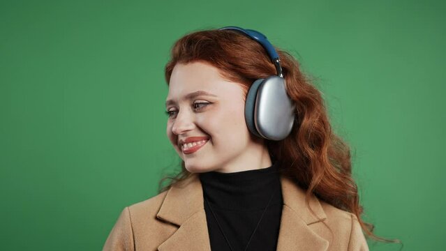 Happy cute businesswoman listening music, enjoying headphones, green background