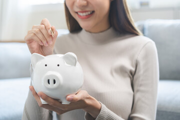 Saving money wealth concept, asian young business woman hand putting coin into piggy for saving...