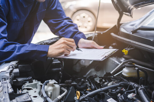 Auto check, car service shop concept. Automobile repairman writing job checklist on clipboard, mechanic checking engine to estimate repair machine, inspecting maintenance by engineer at vehicle garage