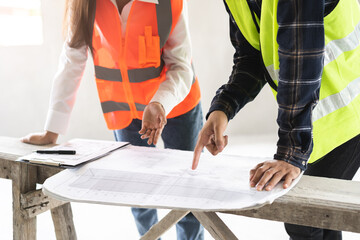 Builder team, two asian young engineer woman, male architect discussing construction on blueprint, follow project to build industrial plan on bench at house site. Engineering worker, teamwork people.