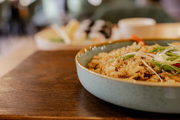 Close up of fried rice with chicken and vegetables served on a blue ceramic plate on wooden table. Asian cuisine, stir fry rice. Copy space