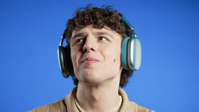Positive curly haired man listening music, enjoying dance with modern headphones