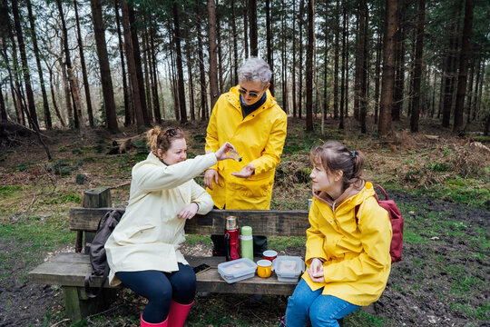 Halt for snack during hiking. Company hikers washing hands with antibacterial sanitizer gel for Hygiene and protection during trip. Friends relaxing and having snack picnic on nature background.